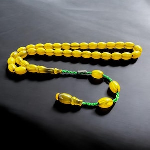 Peut inclure: Un collier de prière en perles jaunes avec un cordon vert et un gland. Les perles sont de forme ovale et ont une finition brillante.