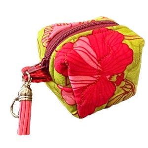 May include: A small, quilted coin purse with a vibrant floral pattern. The purse features a red hibiscus flower design on a lime green background. It has a red zipper and a pink tassel attached to the zipper pull.