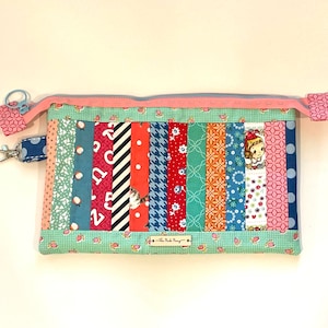 May include: A green and pink patchwork zippered pouch with a variety of colorful fabric strips, including red, orange, yellow, blue, and green. The pouch has a small tag that reads "The Pink Pony".