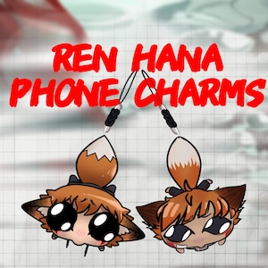 May include: Two cartoon fox phone charms with orange and white fox tails and fox faces with large black eyes. The text "REN HANA PHONE CHARMS" is in red, above the charms.