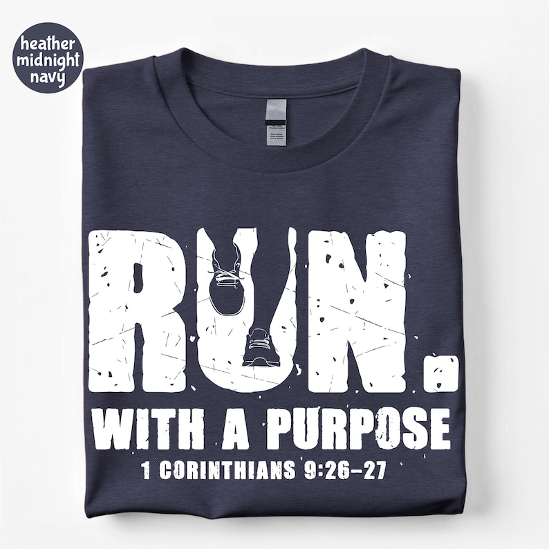 May include: A heather midnight navy t-shirt featuring a white distressed graphic that reads RUN. WITH A PURPOSE 1 CORINTHIANS 9:26-27. The letter U in RUN is replaced by a silhouette of legs and running shoes in a white, weathered, textured font.