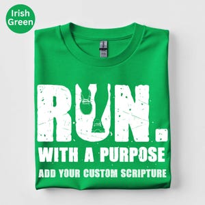 May include: An Irish green short-sleeve t-shirt featuring a white graphic with the text RUN. WITH A PURPOSE and ADD YOUR CUSTOM SCRIPTURE. The letter U in RUN is replaced by a graphic of running legs and trainers. The text has a distressed texture.