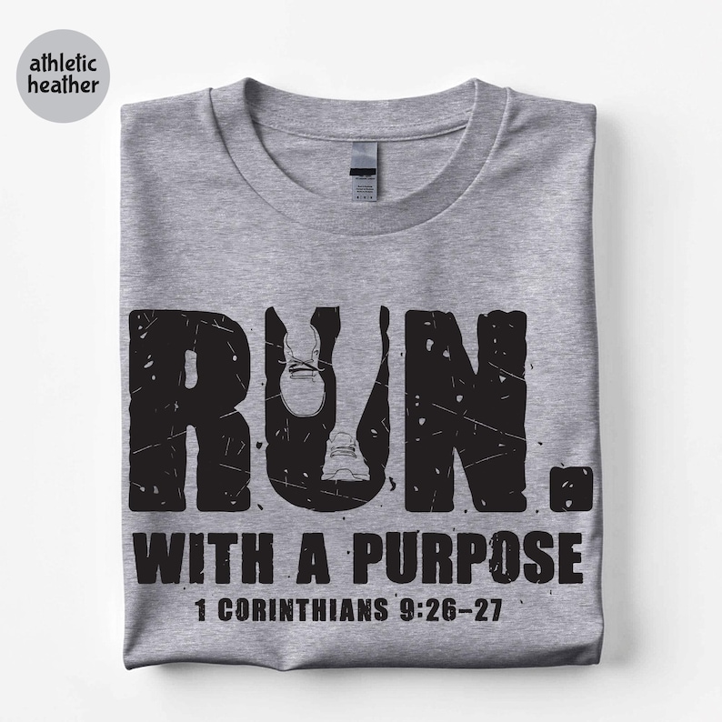 May include: An athletic heather grey t-shirt featuring a black distressed graphic that reads RUN with a shoe icon inside the letter U, followed by the text WITH A PURPOSE and the scripture reference 1 CORINTHIANS 9:26-27 in a bold, sans-serif font.