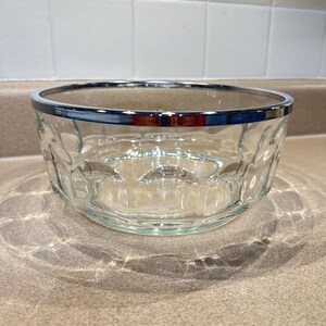 May include: Clear glass bowl with a silver rim. The bowl has a textured, patterned design on the sides. This decorative bowl is suitable for serving salads, fruits, or other dishes.