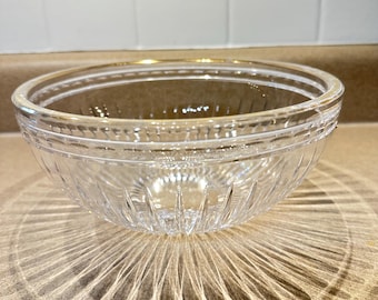Könnte beinhalten: Eine klare Glasschüssel mit einem dekorativen Muster. Die Schüssel hat eine abgerundete Form mit einem leicht ausgestellten Rand. Die Schüssel steht auf einer hellbraunen Oberfläche. Der Schatten der Schüssel ist sichtbar.