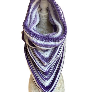 May include: A purple and white crocheted cowl with a hood. The cowl is made with a striped pattern and has a scalloped edge.
