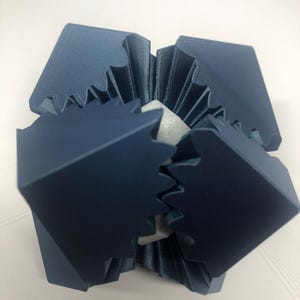 May include: A geometric sculpture with a dark blue exterior and a light gray interior. The exterior is composed of angular, interlocking shapes, creating a complex, multi-faceted design. The sculpture appears to be made of a rigid material.