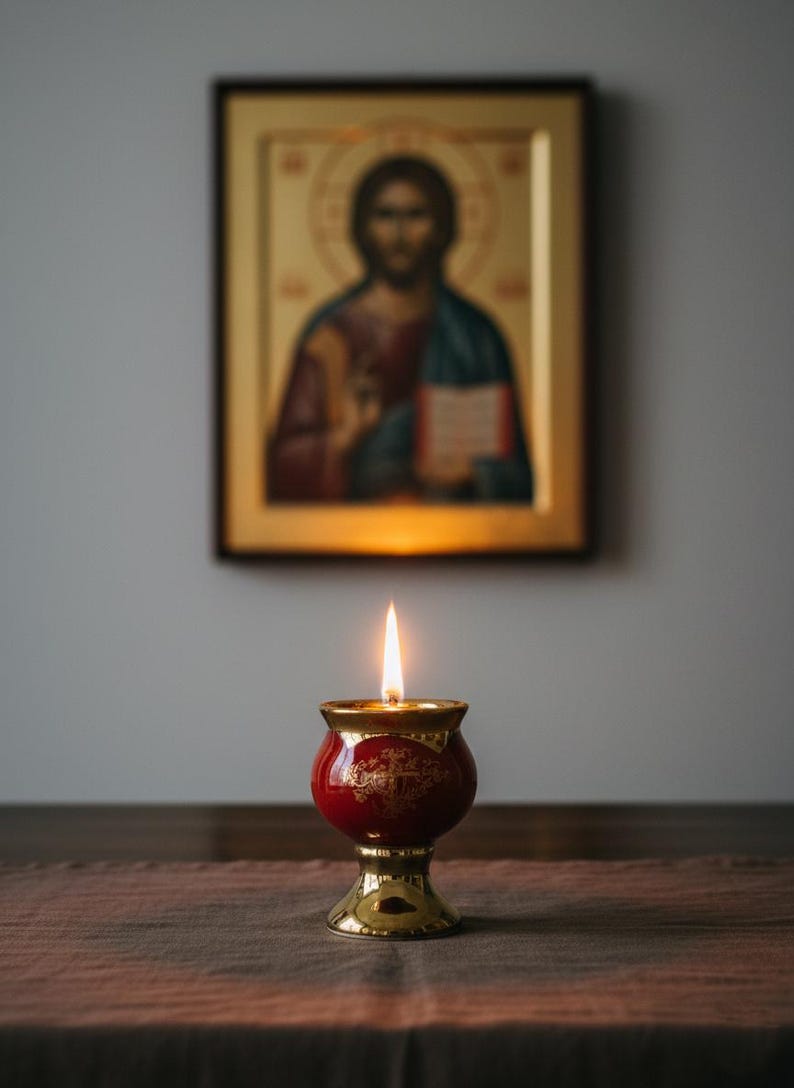May include: A lit red and gold candle holder with a flame, set against a blurred background of a religious icon. The candle holder has a detailed design and sits on a wooden surface.