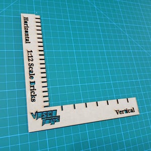 Può includere: Un righello di legno con una scala orizzontale etichettata "Horizontal 1:12 Scale Bricks" e una scala verticale etichettata "Vertical". Il righello è su un tappetino da taglio verde.