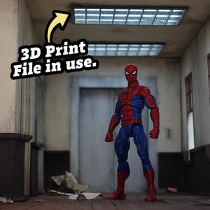 Puede incluir: Una figura de acción de Spider-Man con un traje rojo y azul está de pie en una habitación con poca luz. La figura está posada con los brazos a los lados. El texto de la imagen dice "3D Print File in use."