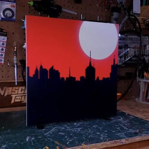 May include: A black cityscape silhouette against a red background with a white circle in the upper right corner.