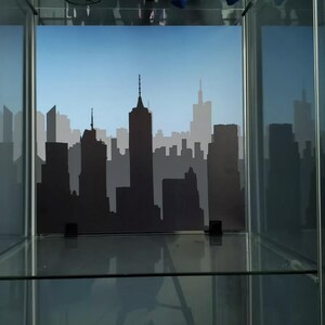 May include: A glass display case with a black silhouette of a city skyline against a blue sky background.