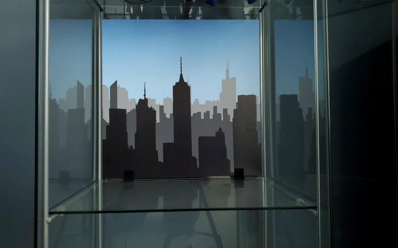 May include: A glass display case with a black silhouette of a city skyline against a blue sky background.