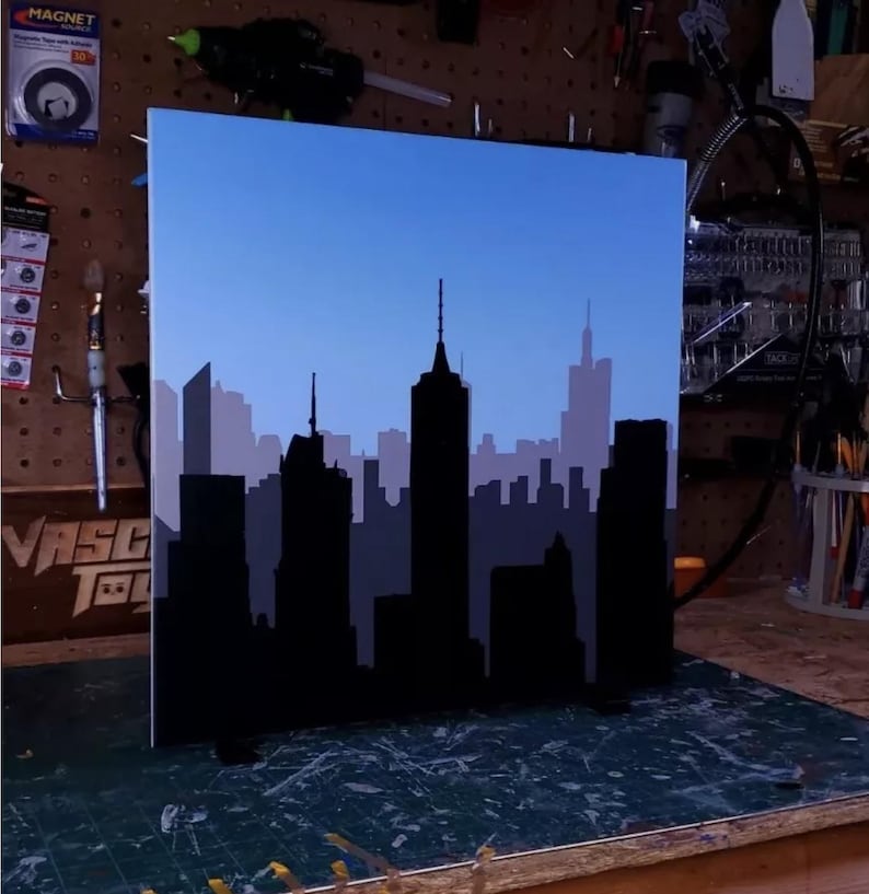 May include: A black silhouette of a city skyline against a blue sky. The skyline is painted on a white board.