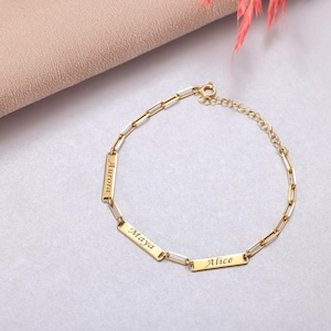 May include: Gold chain bracelet with three rectangular charms engraved with the names "Aurora", "Maya", and "Alice".