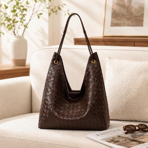 May include: A dark brown hobo bag featuring an intricate woven pattern across its entire surface. The bag has a slouchy, triangular silhouette with two thin shoulder straps attached to gold-toned metal grommets at the top opening of the bag.