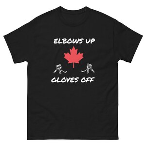 Könnte beinhalten: Schwarzes T-Shirt mit dem Text "ELBOWS UP" über einem roten Ahornblatt und dem Text "GLOVES OFF" darunter. Zwei Eishockeyspieler-Figuren befinden sich auf beiden Seiten des Ahornblatts.