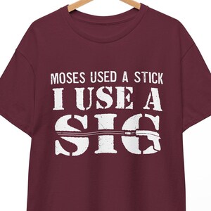 Puede incluir: Camiseta color burdeos con texto blanco que dice "Moses used a stick I use a SIG" con un gráfico de una pistola.