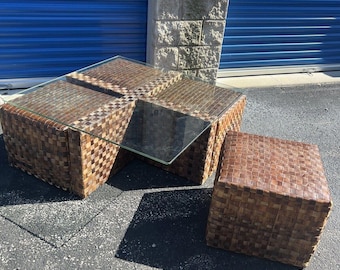 May include: A set of four woven brown wicker cube ottomans with a glass top coffee table. The ottomans can be used as individual seats or combined to create a larger coffee table.
