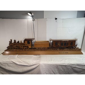 May include: A detailed wooden model train set, featuring a locomotive, tender, and passenger car. The train is crafted from light-colored wood and sits on a wooden track. The model includes intricate details, such as wheels, windows, and a roof. The text on the base reads "HIGH YORK GOLDEN RUSH".