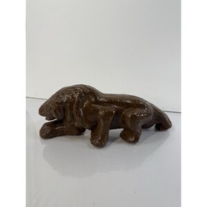 May include: A brown, textured lion figurine in a resting pose. The sculpture is a solid color and appears to be made of a heavy material. The lion's features are detailed, with visible paws and a mane.