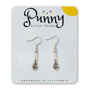 May include: Silver-colored microphone earrings on a white card with the text "Punny Little Things" and "Handmade in California". The earrings have a hook design and are shaped like miniature microphones.
