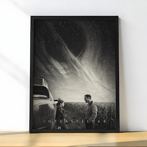 May include: Monochrome framed print of the film Interstellar. The image depicts two figures in a field, with a car and a dramatic sky featuring a celestial body. The word "INTERSTELLAR" is printed at the bottom of the image.