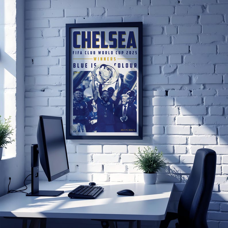 May include: A framed poster with the word "CHELSEA" in large blue letters. The poster commemorates the FIFA Club World Cup 2025 winners. The image shows a team celebrating with a trophy. The poster is hanging on a white brick wall.