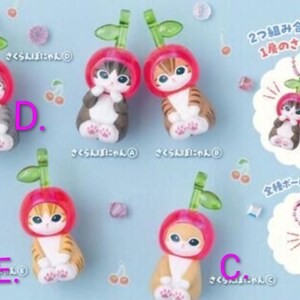 May include: Five small cat figurines, each wearing a red cherry-shaped hood with a green stem and leaf. The cats have various fur patterns and colors. A measurement indicator shows a height of 4.3 cm. Includes pink ball chains for hanging.