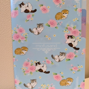 May include: A light blue file folder decorated with cartoon kittens, pink roses, and yellow flowers. The folder features the text "mofusand" in a decorative font and a decorative border.