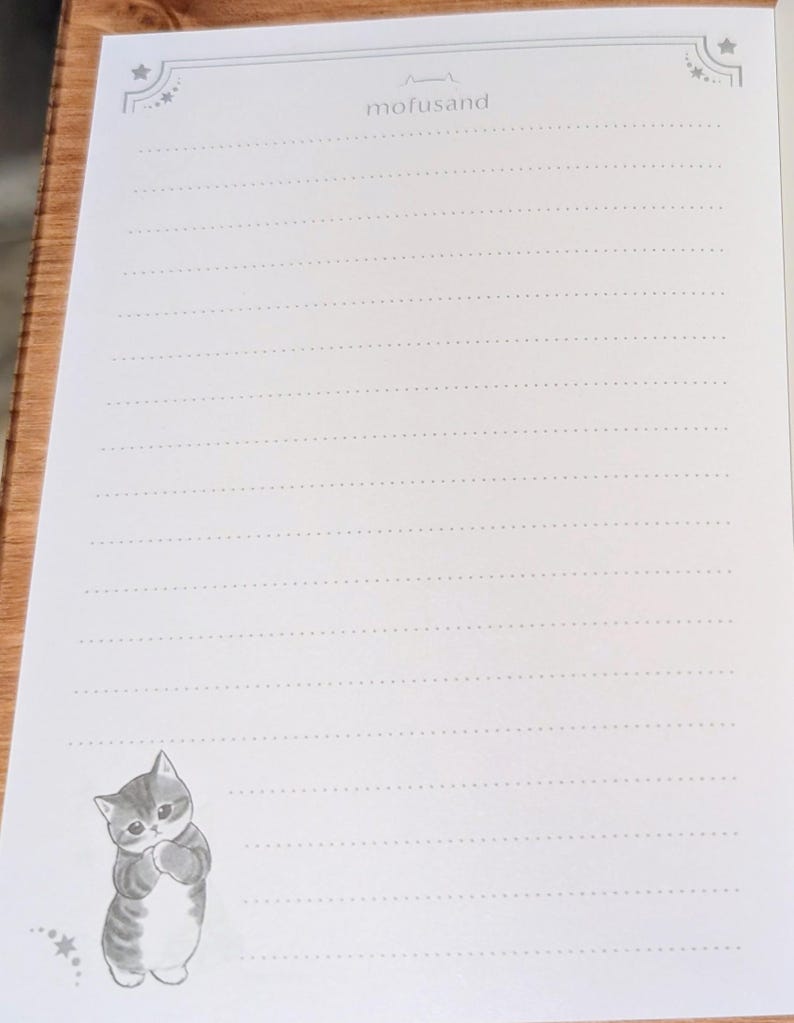 May include: White lined stationery paper with a cute gray and white cat illustration in the bottom left corner. The text "mofusand" is printed at the top center. Decorative star and dot designs are in the corners.