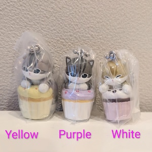 K&ouml;nnte beinhalten: Drei katzenf&ouml;rmige Figuren in Plastikverpackung. Jede Katze sitzt auf einem Cupcake. Die Cupcakes sind gelb, lila und wei&szlig;. Der Text "Yellow", "Purple" und "White" befindet sich darunter.