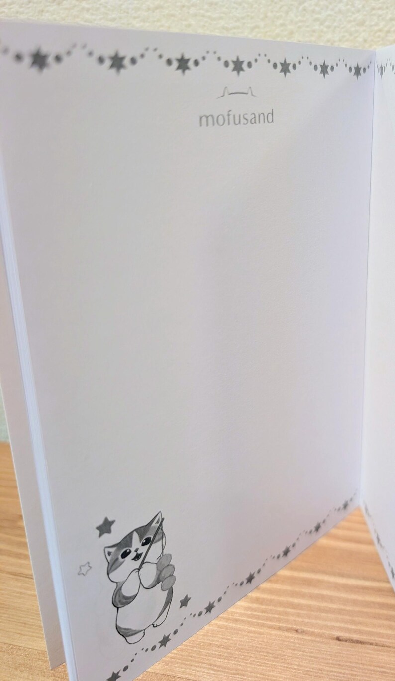 May include: Open notebook with blank white pages. The notebook features a decorative border of stars and a cartoon cat illustration. The word "mofusand" is printed at the top of the page.