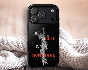 May include: Black phone case with a design featuring a sword, roses, and the text "LIKE A ROSE IN A GRAVEYARD" in white and red. The case has a glossy finish and a camera cutout.