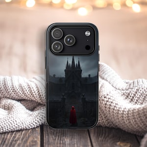 Op de afbeelding: Zwarte telefoonhoes met een gotische illustratie van een donker kasteel onder een bewolkte hemel. Een persoon in een rode cape staat voor de kasteelpoorten. De hoes heeft een zwart frame en een glanzende afwerking.