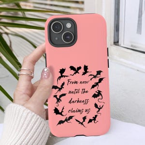 May include: A pink phone case with a black camera module and black accents. The case features a circular arrangement of black dragon silhouettes around the text "From now until the darkness claims us."