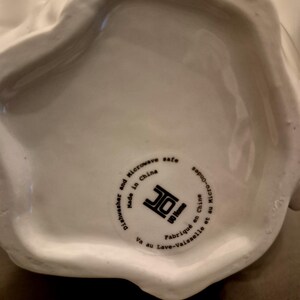 May include: A white ceramic serving dish with a rounded shape. The bottom of the dish has a circular sticker with text that reads "Dishwasher and Microwave safe Made in China UO Home Va au Lave-vaisselle et au Micro-Onde Fabriqu&eacute; en Chine."