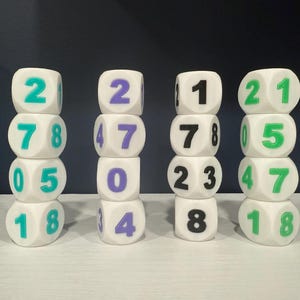 May include: Four stacks of white dice with coloured numbers. The dice have teal, purple, and green numbers. Each stack has four dice, with the numbers arranged vertically. The background is a dark blue.