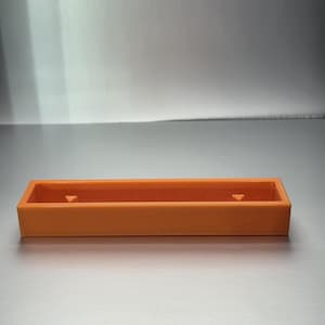 May include: An orange rectangular tray with a low profile. The tray has a smooth surface and two small, triangular cutouts on the inside of the long sides. The tray is made of a solid, opaque material.