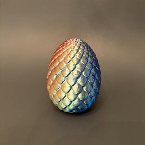 May include: A decorative egg with a textured, scaled surface. The egg transitions in color from orange to blue, with a metallic sheen. The egg is an oval shape and is a fantasy-themed item.