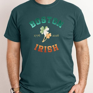 May include: Teal green t-shirt with the words "BOSTON IRISH" in gradient green and orange lettering. A shamrock graphic is centered above the year dates 1776 and 2026. The shirt is a crew neck style.