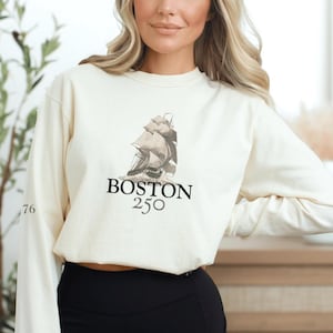 May include: Cream-colored sweatshirt with a graphic of a sailing ship and the text "BOSTON 250". The number "76" is printed on the left sleeve. The sweatshirt is long-sleeved.