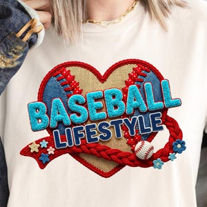 May include: A cream-colored t-shirt featuring a heart-shaped design with a baseball theme. The design includes the words "BASEBALL LIFESTYLE" in blue, a baseball, and decorative elements. The shirt is made of a soft material.