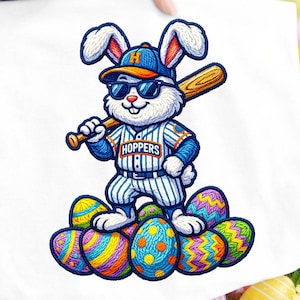Può includere: Borsa tote bianca a tema pasquale, raffigurante un coniglio che gioca a baseball con occhiali da sole e una divisa. Il coniglio tiene in mano una mazza e si trova su un mucchio di uova di Pasqua decorate. La parola "HOPPERS" è sulla divisa.