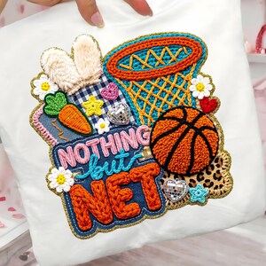 May include: White pillow with an embroidered basketball-themed design. The design includes a basketball, net, bunny ears, carrot, and the words "NOTHING but NET". Accents include flowers, hearts, and stars.