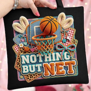 May include: Black tote bag featuring a basketball-themed design with the text "NOTHING BUT NET." The design includes a basketball, hoop, and bunny ears, with denim, leopard print, and gingham accents. The bag is held by a person.