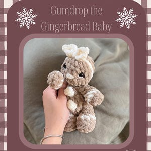以下が含まれることがあります： 「Gumdrop the Gingerbread Baby」の文字が入った、人が持っているかぎ針編みのジンジャーブレッドベビー人形。人形は茶色と白で、白いアクセントが付いています。画像には「No Sew!」と「Crochet pattern by」の文字が含まれています。