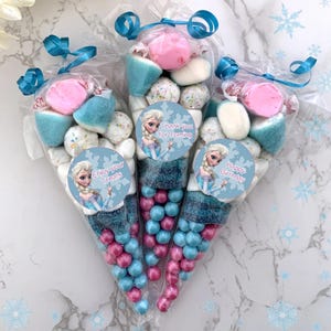 May include: Three clear plastic cones filled with various candies, including pink and blue candies, white marshmallows, and sprinkles. Each cone has a round sticker with a picture of Elsa from Frozen and text that says "Thank you for coming", "Enjoy your treats", and "Happy Birthday".