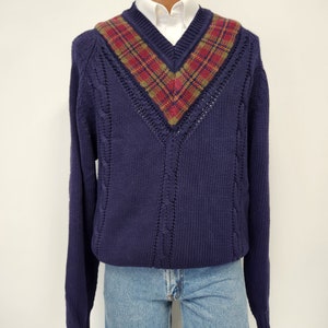 May include: A navy blue v-neck sweater with a cable knit pattern and a plaid trim around the neckline.