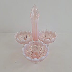 May include: A pale pink opalescent glass centrepiece featuring a central tall, fluted vase surrounded by three matching scalloped bowls. The glass has a translucent, milky finish with vertical ridges and a delicate, petal-like edge design.